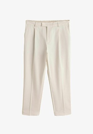 Személy bézs pliszírozott nadrágban és zöld csíkos ingben, szabadban egy medence közelében áll, a kezei lazán a test mellett.