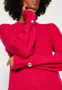 Fuchsia wollen blend trui met textuur breisel, aansluitend ontwerp en unieke lange mouwen met kristallen knoopaccenten bij de manchetten.
