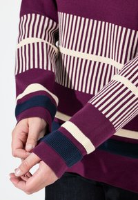 Maglione a pullover di un profondo viola con motivi a righe orizzontali in crema e blu navy. Presenta polsini a costine e una texture di maglia strutturata.