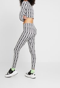 Svartvita leggings med vertikala varumärkesränder, tillsammans med en matchande croppad topp. Har en kroppsnära design och elastisk midja.