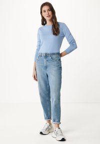 Top a maniche lunghe ribbed blu chiaro abbinato a jeans blu chiaro a vita alta e leggermente morbidi. Indossato con scarpe da ginnastica bianche e grigie.