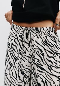 Zwart-witte zebra print broek van lichtgewicht stof met een elastische tailleband en trekkoord, voorzien van zijzakken en een relaxte pasvorm.