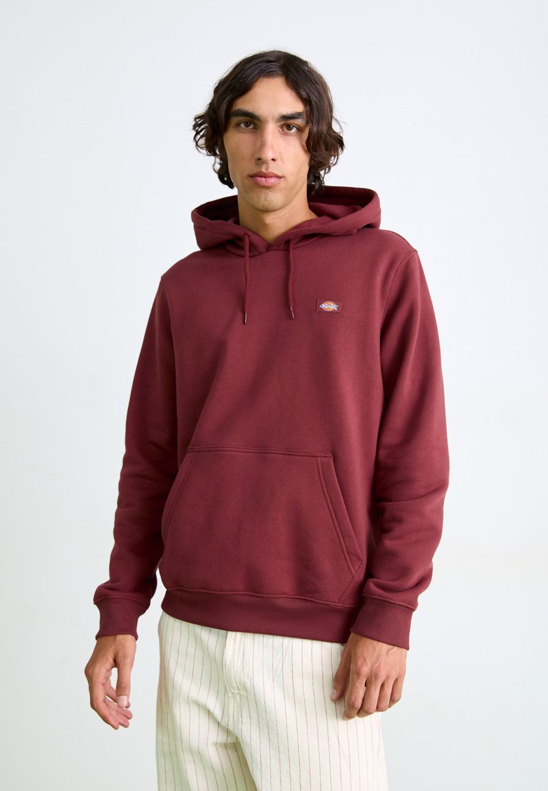 Hoodie bordeaux en coton doux, avec une poche kangourou à l'avant et une capuche avec cordon de serrage. Petite étiquette avec logo sur la poitrine. Manches ajustées.