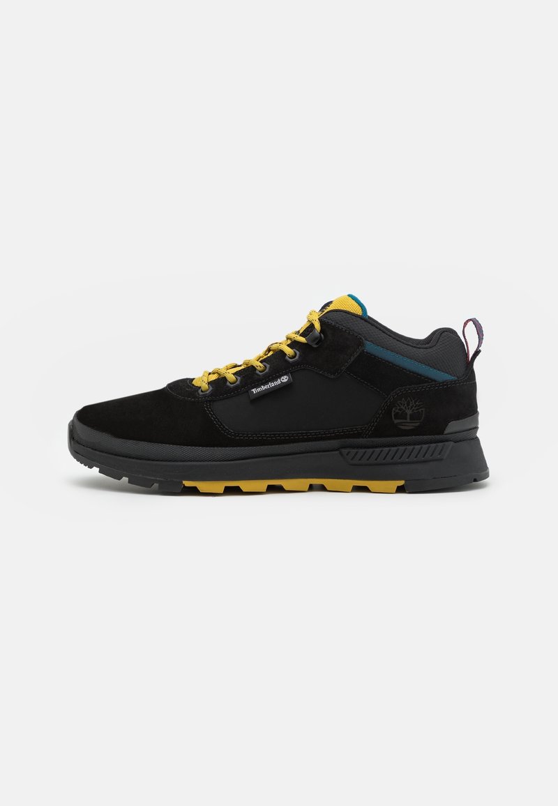 Chaussure de randonnée en suède noir avec des lacets et des accents jaunes, dotée d'une semelle en caoutchouc noir robuste et d'un panneau latéral texturé. Logo Timberland visible.