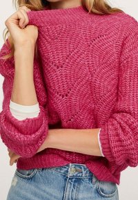 Pull tricoté rose à col montant et coupe ample. Caractérisé par des motifs texturés, des poignets roulés et une chemise blanche superposée en dessous.