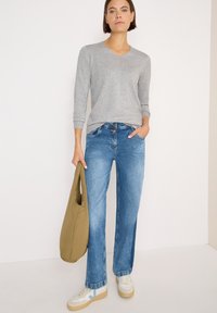 Grå långärmad V-ringad tröja, blå raka jeans, vita sneakers med blå detaljer och en mjuk olivgrön toteväska.