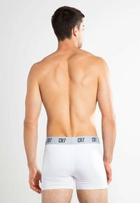 White boxer briefs with a grey elastic waistband featuring "CR7" logo. Smooth material, fitted design, and mid-thigh length.
