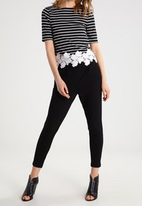 Mustavalkoinen raidallinen paita, jossa on kukkakuvioinen pitsireuna, yhdistettynä mustiin slim-fit-housuihin ja avokärkisiin mustiin nilkkabootseihin.