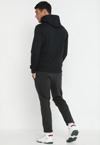 Sudadera negra con bolsillo tipo canguro, puños acanalados y cintura; combinada con pantalones deportivos gris oscuro y zapatillas blancas con acentos rojos y verdes.