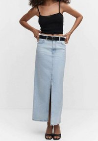 Jupe maxi en denim bleu clair avec une fente frontale, associée à un top court noir et une ceinture noire. Elle présente un design classique à cinq poches.