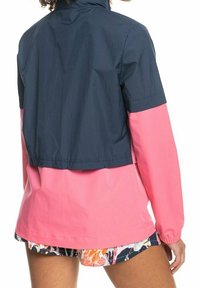 Giacca impermeabile con la parte superiore blu marina e la parte inferiore rosa. Presenta maniche corte e una vestibilità morbida. Tessuto liscio.