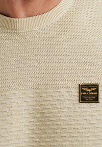 Beige gestructureerde trui met een geribbelde ronde hals. Beschikt over een zwart-geel logo label met de tekst "PME LEGEND."
