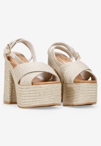 Beige platform sandals with braided rope material and a chunky heel. Open-toe design with crisscross straps and an ankle buckle closure.