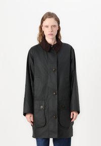 Casaco verde escuro com botões, gola em veludo cotelê castanha e dois bolsos frontais. Apresenta um corte direito e mangas longas.