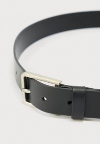 Juodos odos diržas su sidabrine stačiakampės formos sagtimi ir keliomis reguliavimo skylutėmis ant balto fono.