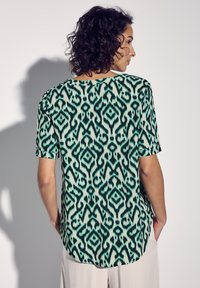 Top a maniche corte in tessuto verde chiaro con un audace motivo ikat verde scuro. Orlo arrotondato e vestibilità rilassata con polsini delle maniche arrotolati.