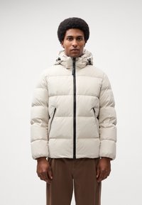 Light beige padded jacket with a hood, featuring zippered pockets and black accents. Textured, quilted design for insulation.