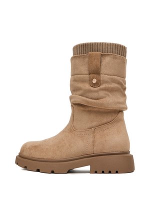 Beżowy zamszowy but do połowy łydki z prążkowanym dzianinowym mankietem, pętelką do zakładania, zaokrąglonym noskiem i masywną gumową podeszwą z głębokim bieżnikiem zapewniającym przyczepność.