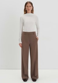 Weißes Langarmoberteil kombiniert mit taillierten, weit geschnittenen braunen Hosen mit hoher Taille. Glatte Textur, maßgeschneiderte Passform, mit Taschen und minimalistischer Gestaltung.