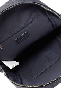 Interno di uno zaino in pelle nera con una tasca con cerniera, foderato in tessuto liscio, e un'etichetta piccola. Gli accenti in cerniera dorata completano il design.