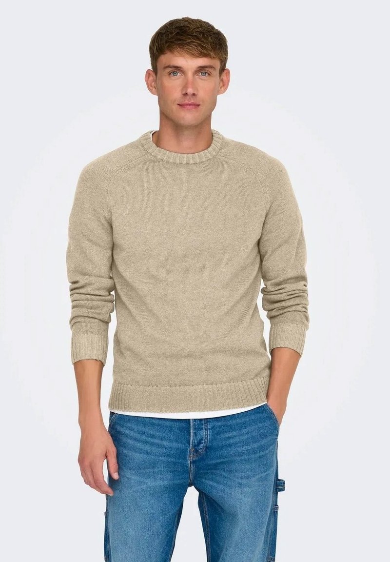 Maglione beige a maglia con scollatura e polsini a coste, caratterizzato da un design pulito e una vestibilità regolare, indossato sopra dei jeans blu.