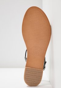 Semelle de sandale en cuir avec une surface texturée couleur tan. Caractéristiques de marquage à chaud de la marque et indication de taille. La forme est ovale avec un motif de semelle ondulé.