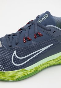 Gros plan d'une chaussure de trail bleu marine avec des lacets rouges, un logo Swoosh blanc et une semelle texturée verte étiquetée Trail n° 440.