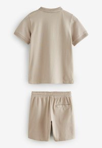 Beige Baumwoll-T-Shirt mit kurzen Ärmeln und geripptem Kragen, kombiniert mit passenden Shorts, die einen elastischen Bund und eine Gesäßtasche haben.