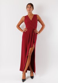 Abito bordeaux con scollatura a V profonda, design senza maniche e spacco alto alla coscia. Realizzato in un tessuto morbido, abbinato a tacchi alti neri.