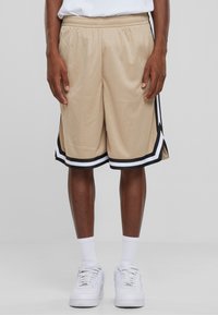 Shorts en mesh beige avec des bandes latérales noires et blanches, dotés d'une taille élastique et de fentes latérales pour la ventilation.