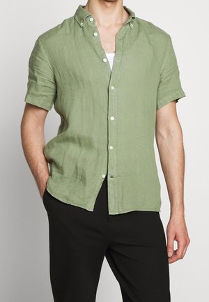 Chemise à manches courtes, déboutonnée en lin vert clair. Dispose d'un col pointu et d'une patte de boutonnage à l'avant avec des boutons blancs. Tissu texturé.