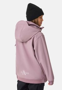 Jasnoróżowa bluza z dużym kapturem i prążkowanymi mankietami, z białym logo na plecach. W połączeniu z czarną dzianinową czapką beanie.