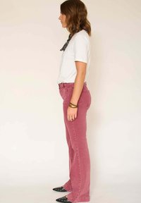 Jean en denim rose évasé avec une taille haute, poches avant et arrière ; associé à un t-shirt blanc et des chaussures noires à bout pointu.
