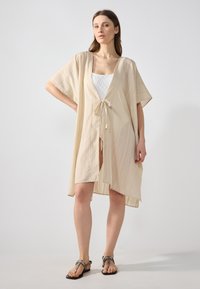 Beige auki kimono dengan lengan pendek, dilengkapi dengan penutupan tali di pinggang, garis vertikal, dan kain yang ringan.