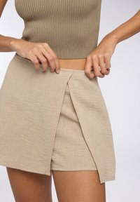 Skort beige in lino con finitura testurizzata, caratterizzato da un design avvolgente, vita alta e cuciture visibili vicino all'apertura.