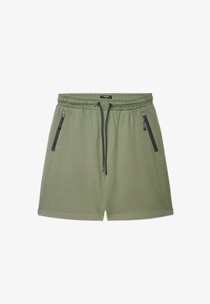 Shorts casual verde chiaro con vita elastica, coulisse nere e due tasche frontali con zip, distesi su uno sfondo bianco.
