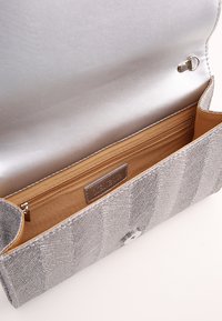 Sølv tekstureret clutch taske med en glat metallisk indvendig, der har en lynlåslomme og en trykknaplukning. Accenteret med en logo-plade.