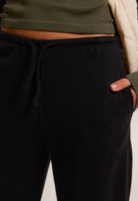 Black sweatpants made of soft fabric with ribbed texture, featuring an elastic waistband and side pockets. Adjustable drawstring detail.