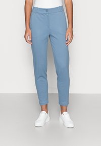 Lichtblauwe, slanke broek met een gladde textuur, voorzien van een knoopsluiting en ceintuurlussen, gecombineerd met witte sneakers.