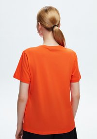 Camiseta corta de manga corta color naranja con escote redondo. Fabricada con tela suave, presenta un corte relajado. Sin logotipos ni patrones visibles.