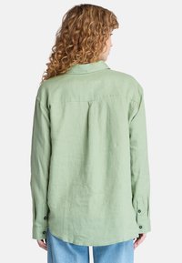 Camicia a maniche lunghe verde chiaro in lino. Presenta un colletto button-down, una piega sul retro e polsini con bottoni. texture morbida, vestibilità rilassata.