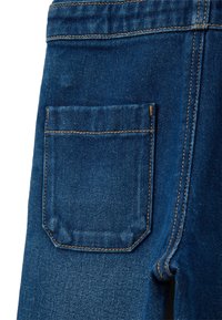Dunkelblaue Jeansstoff verfügt über eine Gesäßtasche mit kontrastierendem braunem Nähten und einer sauberen Kante; die Textur ist glatt mit leichter Maserung.