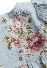 Vaaleansininen kangas, jossa on kukkakuosi, jossa on vaaleanpunaisia ja vihreitä kukkia. Mukana puunappit ja karheus pinta.