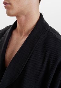 Bata negra con textura de waffle y cuello de chal, con un corte holgado y un escote en V profundo, que presenta una tela suave y una costura mínima.
