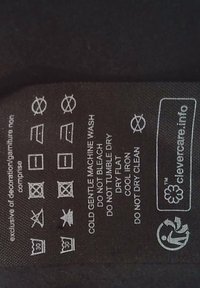 Etichetta di cura in tessuto nero con simboli di lavaggio bianchi. Le istruzioni includono lavaggio delicato in lavatrice, non candeggiare e stiratura a freddo. Include il logo.