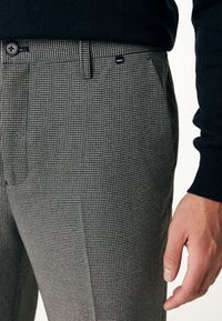 Šedé kostkované kalhoty vyrobené z texturované tkaniny. Mají zapínání na knoflík a boční kapsy. Jsou vybaveny malou značkovou cedulkou.