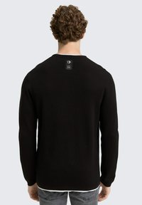Schwarzer, gestrickter Pullover mit langen Ärmeln, runden Ausschnitt und einem kleinen Etikett auf der Rückseite. Texturiertes Material mit einer taillierten Silhouette.