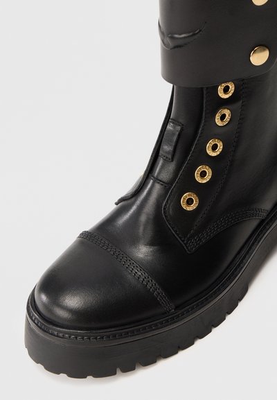 Black leather boot with gold-tone eyelets and hardware. Features a rounded toe and textured sole. Ankle-height with a smooth finish.