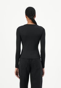 Black long-sleeve top with a fitted design and round neckline, made of smooth fabric, paired with high-waisted dark denim jeans.