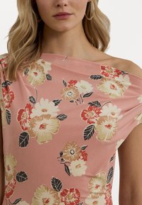 Off-the-shoulder kjole i rosa stoff med blomstermønster som har røde, kremfargede og svarte blomster samt grønne blader. Glatt tekstur.